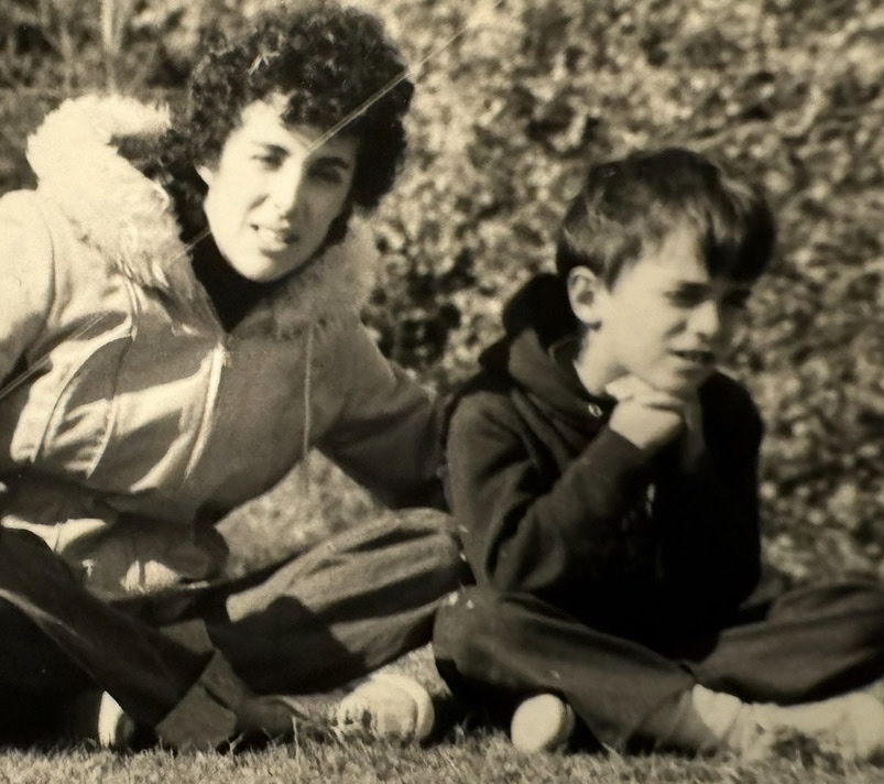 A young Anthony Castore sitting on the grass with his mother in a vintage black-and-white photograph.